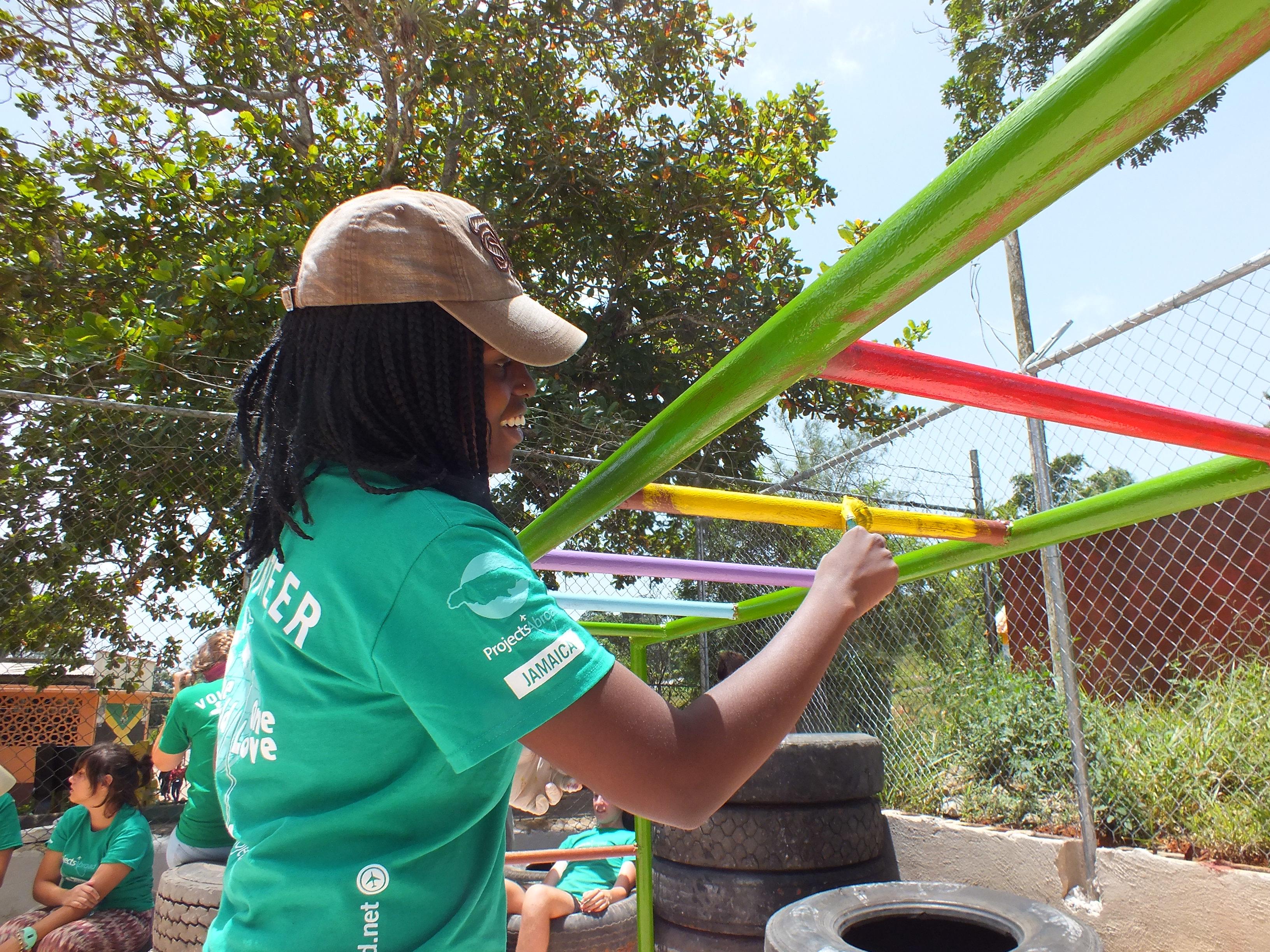 A volunteer paints playground equipment during her international volunteer trip to Jamaica, in the Caribbean. A female Projects Abroad volunteer helps refurbish playground equipment in Jamaica as part of her summer volunteer abroad program.